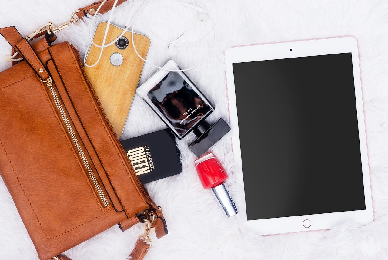 Stylish flat lay featuring gadgets, cosmetics, and a leather bag on a plush surface.